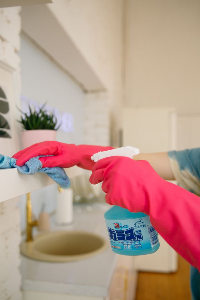 services-01 Person using spray bottle and cloth for cleaning a kitchen shelf, ensuring hygiene and cleanliness.